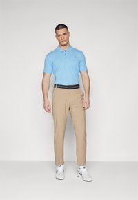 Svijetloplavi polo majica s kratkim rukavima s tri gumba, kombinirana s bež hlačama i bijelim sportskim cipelama s crnim naglasima.