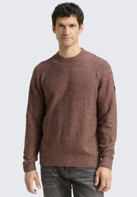 Pull en maille marron texturé avec un col ras du cou. Présente un motif subtile, des manches longues et des poignets côtelés. Inclut un accent noir sur la manche.