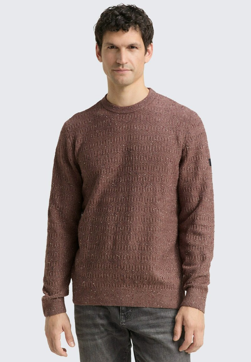 Pull en maille marron texturé avec un col ras du cou. Présente un motif subtile, des manches longues et des poignets côtelés. Inclut un accent noir sur la manche.