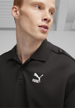 Sort polo shirt med et tekstureret stof, der har et hvidt Puma-logo på venstre bryst og et klassisk kravedesign.