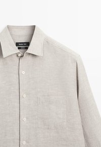 Chemise en lin beige clair à manches longues avec poche avant, fermeture par boutons et col classique, étiquette Massimo Dutti.