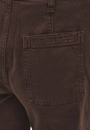 Primer plano de un bolsillo trasero de mezclilla marrón con costuras visibles en un par de pantalones.