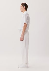 T-shirt bianco a maniche corte abbinato a pantaloni in denim bianchi e sneakers bianche. Design semplice con vestibilità comoda e silhouette pulita.