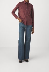 Bordowa koszula z długim rękawem, kołnierzykiem na guziki i kieszenią na piersi, zestawiona z szerokimi, niebieskimi jeansami o prostych nogawkach. Gładka tekstura, dopasowany krój.