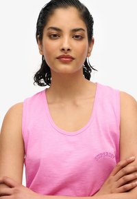 Top de algodón rosa sin mangas con un escote redondo. Cuenta con un pequeño logo bordado de "Superdry" en el pecho. Textura suave.
