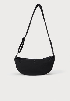 Sac bandoulière noir en forme de croissant, avec sangle réglable, petit logo à l'avant et un design simple et lisse sur fond uni.