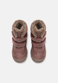 Brązowe syntetyczne bootsy z miękkim, puszystym wyściółką, podwójnymi paskami na rzepy i kontrastującymi czerwonymi przeszyciami. Wytrzymałe gumowe podeszwy. Pokazano widok z góry.