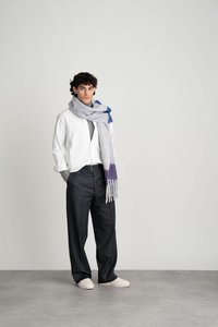 Grijze wol sjaal met blauw en paars verloop, witte overhemden, donkere broek en lichte schoenen. Model staat tegen een neutrale achtergrond.