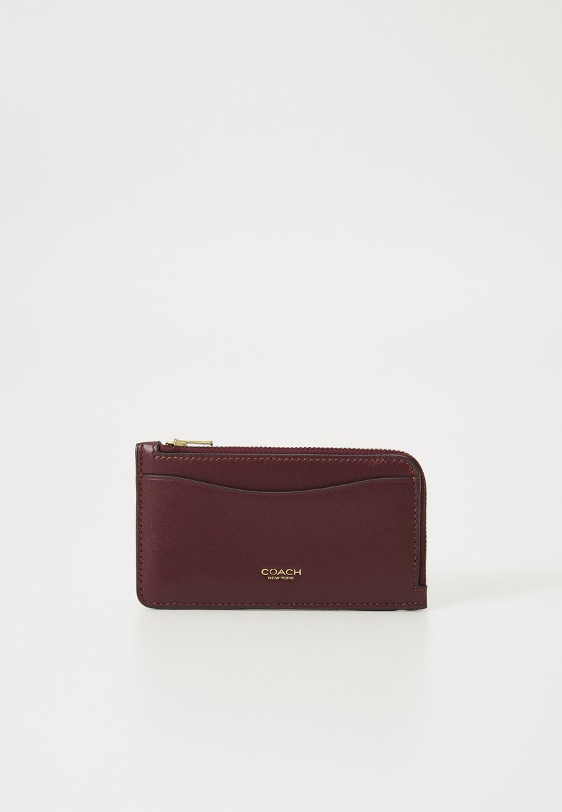 Burgundy leather wallet with a zip closure, featuring a smooth texture and gold "COACH" branding on the front. Simple, rectangular design.