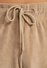 Close-up of beige terry cloth shorts with a tied braided drawstring at the elastic waistband.