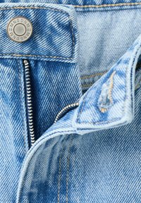 Světle modré džínové kalhoty s částečně rozepnutým stříbrným zipem a kovovým knoflíkem s rytinou "MNGDNM 1984".