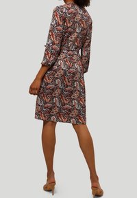 Il vestito presenta un vivace motivo paisley nei colori rosso, blu e beige. Il design include una vita cinchata e maniche a tre quarti.