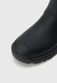 Μαύρο μποτάκι αστραγάλου με στρογγυλεμένη μύτη, κατασκευασμένο από υφή συνθετικού υλικού. Η σόλα είναι παχιά και διαμορφωμένη με σχέδιο για καλύτερη πρόσφυση.