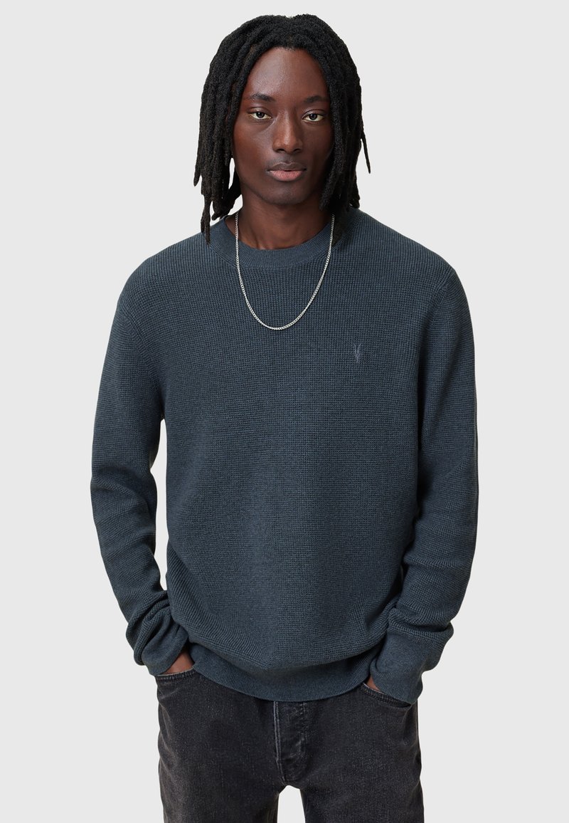 Maglione lavorato a maglia blu scuro con scollatura a girocollo e maniche lunghe. Presenta un motivo testurizzato e un logo discreto sul petto.