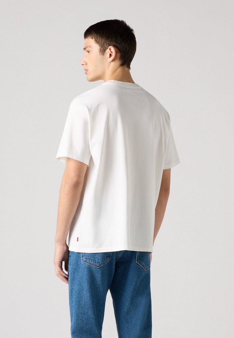 Weißes Baumwoll-T-Shirt mit kurzen Ärmeln und Rundhalsausschnitt, von hinten gezeigt, kombiniert mit blauen Jeans, die ein kleines Logotag haben.