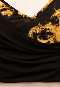 Ένδυμα από μαύρο ύφασμα με χρυσά διακοσμητικά σχέδια σε μπαρόκ στυλ κοντά στη λαιμόκοψη σε σχήμα V και με διπλωτές λεπτομέρειες από κάτω.