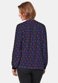 Langearmige blouse met een kleurrijk geometrisch patroon van rood, groen, blauw en paars op een zwarte achtergrond met knoopsmanchetten.