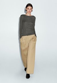Maglia a maniche lunghe grigia scura con scollatura rotonda, abbinata a pantaloni beige a gamba larga e scarpe nere, dotate di tasche laterali e una vestibilità rilassata.