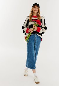 Prúhovaný pletený sveter v čiernej, bielej a červenej farbe, doplnený džínsovou sukňou s prednými gombíkmi a bielymi teniskami s béžovou podrážkou.