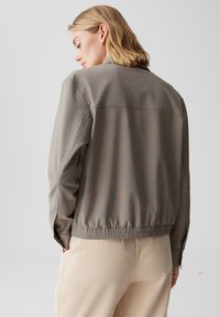 Grijze bomberjack met elastische tailleband, textuurstof en lange mouwen, gecombineerd met crèmekleurige corduroy broeken.
