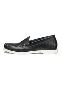 Scarpa slip-on in pelle nera con suola in gomma bianca, cuciture dettagliate e design frontale stile mocassino. Presenta un piccolo logo sul tallone.