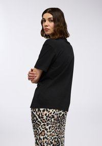 T-shirt nero a maniche corte in cotone, abbinato a una gonna con stampa leopardata, caratterizzata da una texture liscia e una vestibilità rilassata.