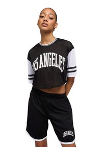 Jersey in rete nero a maniche corte con "LOS ANGELES" in bianco, abbinato a pantaloni corti neri con dettagli bianchi e una vestibilità rilassata.