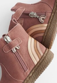 Botine roz din suede, cu dungi bronz, fermoar lateral și talpă din cauciuc texturat. Prezintă o curea din material și accesorii din metal argintiu.