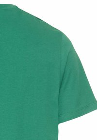 Grøn bomulds t-shirt med rund hals og korte ærmer, der viser en glat tekstur og diskrete søm detaljer ved kanten.