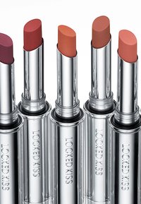 Cinq rouges à lèvres dans des tubes métalliques argentés étiquetés "LOCKED KISS." Les couleurs varient du prune profond au nude. Pointes lisses et arrondies.