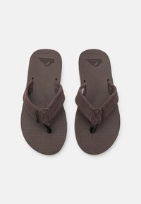 Brown flip-flops with textured rubber soles and soft fabric straps. Features a logo on the footbed and a slightly curved shape for comfort.