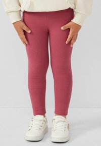 Rosa Baumwolllegging mit tailliertem Schnitt, kombiniert mit weißen Sneakern mit Schnürsenkeln und strukturierter Oberfläche. Einfacher und lässiger Look.