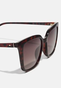 Übergrößige Sonnenbrille mit dunklem Schildpatt-Rahmen, Verlaufslinsen und subtilen goldenen Akzenten an den Scharnieren. Glatte Textur über die gesamte Brille.