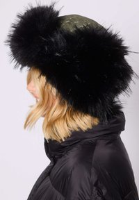 Gewatteerde groene winterhoed met een brede, zwarte nepvachten rand. De hoed wordt gedragen met een zwarte pufferjas, wat een glad oppervlak en textuur laat zien.