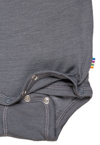 Grauer Baumwollbody mit Druckknöpfen am Boden, ausgestattet mit einem regenbogenfarbenen Etikett an der Seite und einer glatten, weichen Textur.