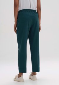 Pantalones teal con un corte relajado, cinturilla elástica y costuras laterales. Combinados con zapatillas blancas, presentan un corte recto y dobladillos acampanados.