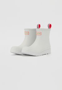 Bottes de cheville en caoutchouc gris avec une semelle blanche, dotées de languettes de tirage rayées rouges et noires et d'une étiquette de logo rouge sur les côtés.
