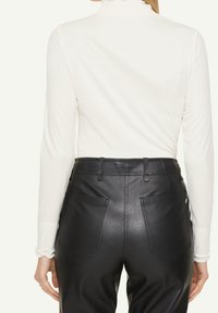 Vitt långärmad topp med hög krage och rynkade detaljer, kombinerat med åtsittande svarta fuskläderbyxor med bakfickor.