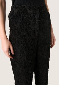 Pantalones negros con textura que presentan un patrón elevado y desgarbado, con una cintura acanalada. La tela parece suave con un detallado intrincado en todo su diseño.