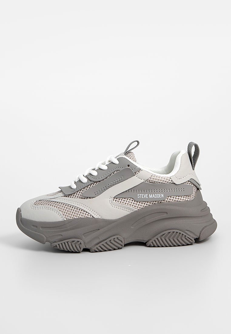 Grå och vita atletiska sneakers med nät- och gummimaterial, tjock sula, snörning fram och framträdande "Steve Madden"-logotyp.