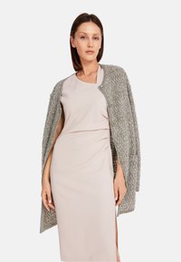 Lichtgrijze, gestructureerde cardigan met een open voorkant, lange mouwen en knopen, gedragen over een lichtroze, aansluitende jurk, wat een gelaagde look toont.