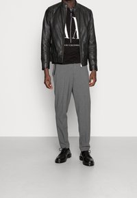 Svart läderjacka med ståkrage, vit grafisk t-shirt under, grå skräddarsydda byxor och svarta läderskor.