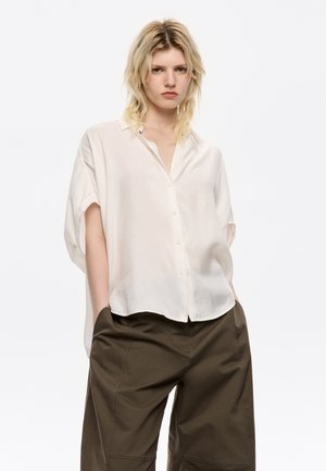 Witte korte mouwen knoopshirt van een lichtgewicht stof, met een relaxte fit en een ronde onderkant, gecombineerd met olijfgroene broek.