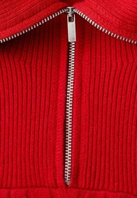 Tejido de rayas rojas con un zipper de metal plateado en el centro, que presenta un alto cuello. La textura parece suave y de punto.