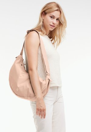 Borsa a spalla beige realizzata in morbido tessuto, con una forma arrotondata, tracolla regolabile e dettagli hardware discreti. Indossata da una modella.