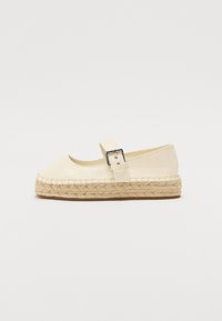 Espadrille crema con punta cerrada, tira al tobillo y hebilla de plata. Suela de yute trenzado con un acabado texturizado. Diseño plano con un detalle mínimo.