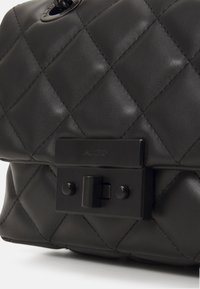 Černá prošívaná kabelka s hladkým koženým povrchem, obdélníkovým tvarem a kovovou sponou s logem.