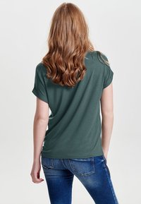 Dark green, short-sleeved t-shirt made of soft fabric, featuring a relaxed fit and rolled sleeves, paired with fitted blue jeans.