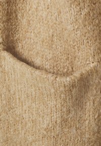 Pletená svetr fabric v světle béžovém tónu, s jemným, texturovaným povrchem a viditelnými vlákny a mírným strečem.