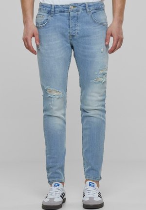 Lyst blå ripped jeans med slim fit, med distressed detaljer og falming, laget av denim. Brukt sammen med hvite og grå sneakers.